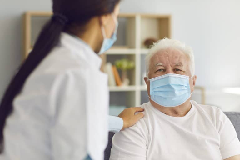 People in protective masks. Woman doctor visits the elderly man and provides him with support and talks to him during the quarantine. Nurse visits a man who is at risk.