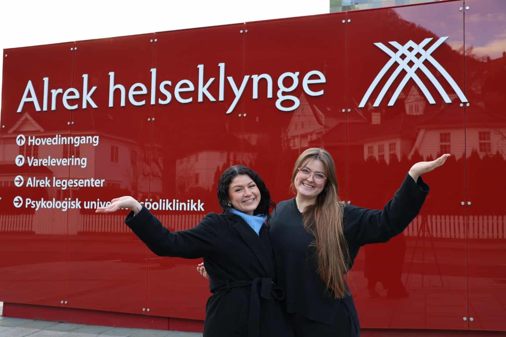 De to nye studentarbeiderne står foran Alrek helseklynge og ønsker velkommen med en inviterende håndgest og smil